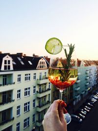 Cropped image of man holding sangria by city against clear sky