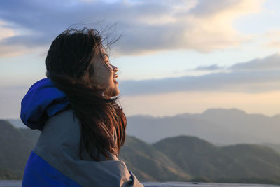 Side view of young woman against sky during sunset