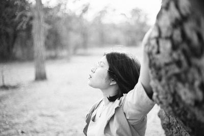 Close-up of woman with closed eyes standing by tree trunk