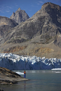 Man standing at the water's edge of a fjord in greenland