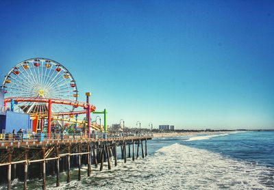 Ferris wheel at beach against clear blue sky