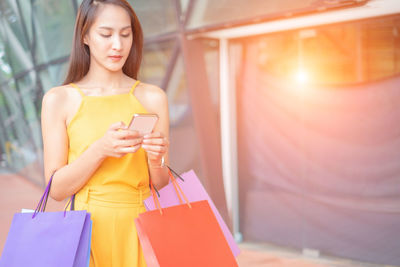 Young woman looking at camera while standing on mobile phone