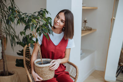 Young woman sitting at home with home potted plant in her hands