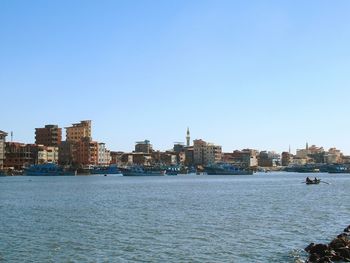 Sea by buildings against clear blue sky