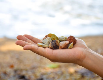 Close-up of hand holding stones against sky