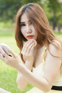 Close-up of young woman applying make-up while sitting outdoors