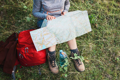 Woman with backpack having break during trip in mountains looking at map sitting on grass