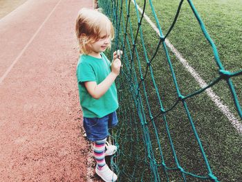 Side view of smiling girl standing by net in playground