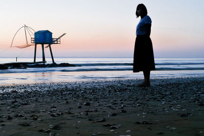 Rear view of man standing at beach during sunset