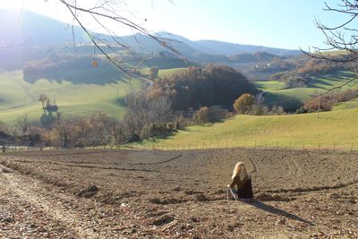 Woman sitting on agicultural landscape against sky