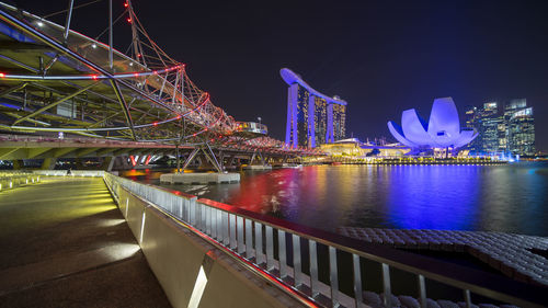 Illuminated bridge over river against buildings at night