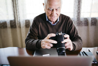 Senior photographer with laptop and digital camera at home