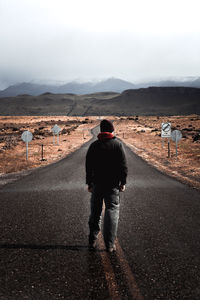 Rear view of man walking on road against sky