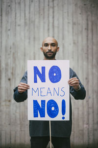 Portrait of male activist holding no means no poster against against wall