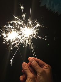 Cropped hands holding illuminated sparklers at night