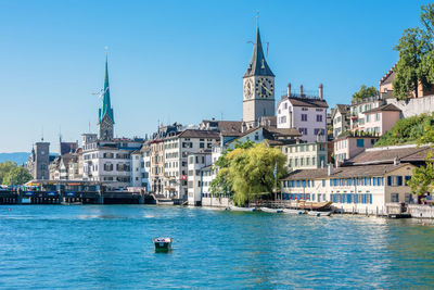 Sailboats in canal amidst buildings in city against clear blue sky