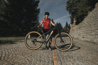 Smiling woman with bicycle standing on cobbled road