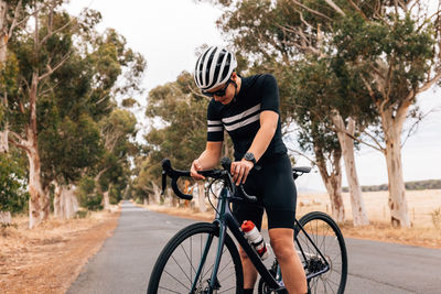 Woman resting while standing with bicycle on road