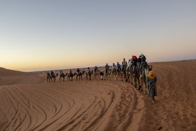 People riding motorcycle in desert against sky during sunset