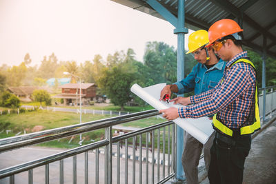 Engineers examining blueprint while standing on footbridge 