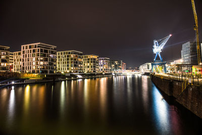 Illuminated buildings by river against sky at night