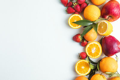 Flat lay of citrus fruits like lime, orange and lemon with leaves on light colored background.