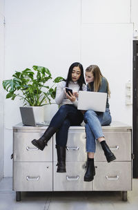 Female bloggers using smart phone while sitting on sideboard in creative office