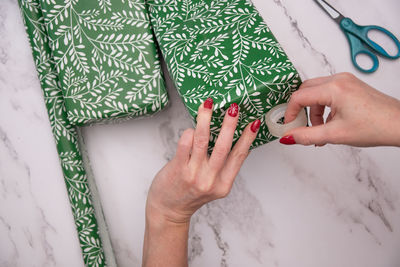 Woman's hands with red christmas manicure wrap gifts in green wrapping paper