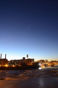 Illuminated city by sea against clear sky at night