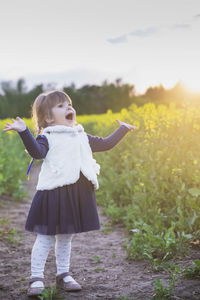 Charming child with ukrainian ribbons in her hair sings in a flowering field at sunset