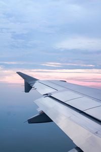 Cropped image of airplane flying against cloudy sky during sunset