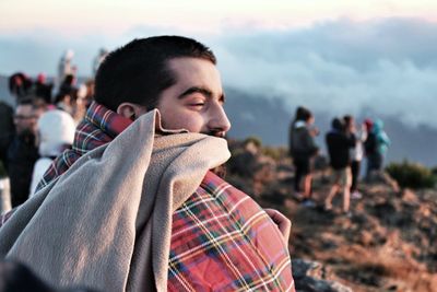 Close-up of young man wearing blanket on cliff during sunset