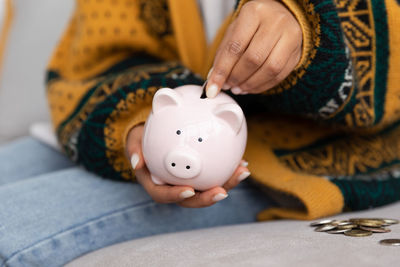 Midsection of woman putting coin in piggy bank