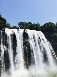 Low angle view of waterfall in forest against clear sky