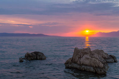 Scenic view of sea and rocks against sky during sunset