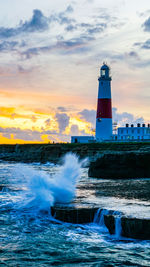 Lighthouse by sea against sky during sunset