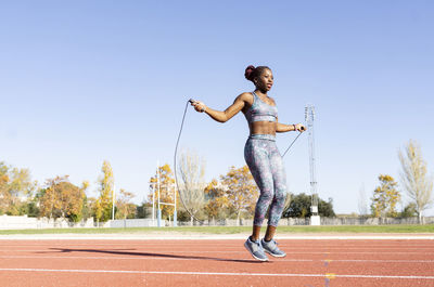 Female sportsperson skipping with jump rope over running track on sunny day