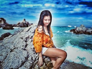 Portrait of smiling young woman on rock at beach