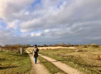 Rear view of man walking on field against sky