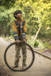 Smiling boy looking away while holding tire on footpath at park