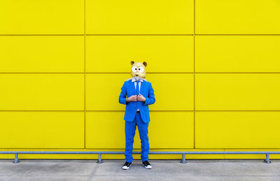 Full length portrait of boy standing against yellow wall