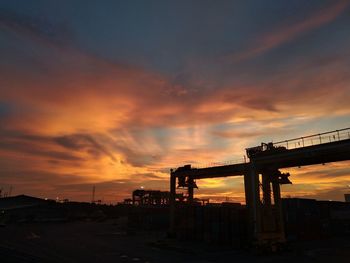 Silhouette of factory against sky during sunset