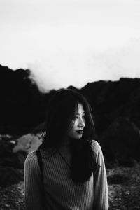 Young woman looking away while standing on land against sky