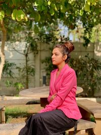 Young woman sitting on bench against plants