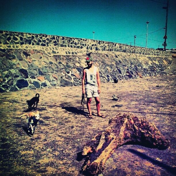 full length, lifestyles, leisure activity, mountain, walking, casual clothing, standing, rear view, sky, blue, dog, landscape, men, sunlight, day, domestic animals, clear sky, rock - object