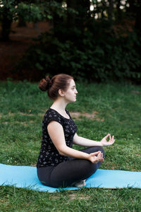 The relaxed girl is doing yoga in the park on carpet