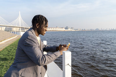 Smiling businessman using smart phone standing by railing