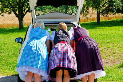 Rear view of women in traditional clothing looking in car trunk at park