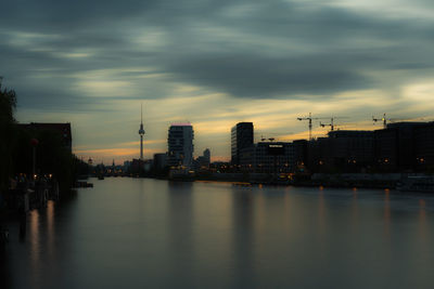 Scenic view of river by buildings against sky at sunset