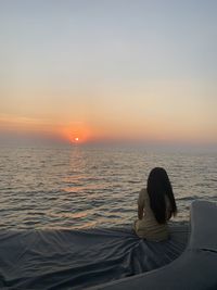 Rear view of woman looking at sea against sunset sky